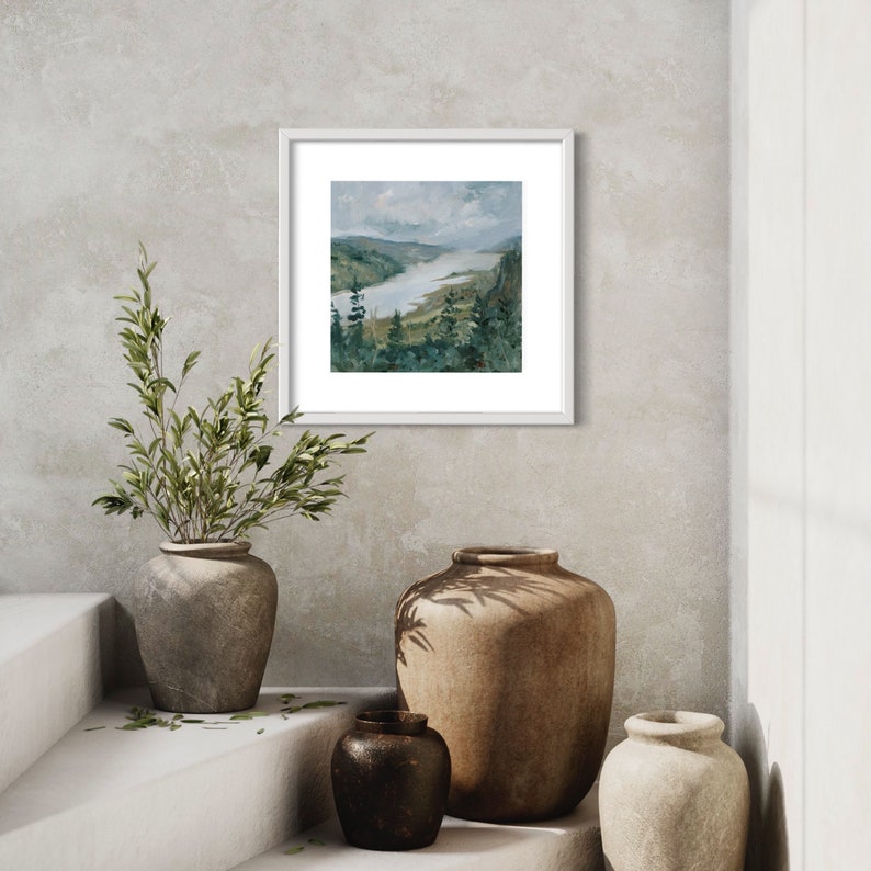 May include: A framed watercolor painting of a river winding through a green valley with trees on the banks. The painting is hanging on a light gray wall with two brown ceramic vases and a smaller black vase on a white shelf below.