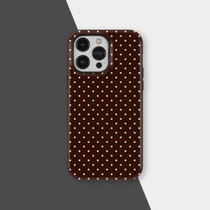 Może przedstawiać: Brązowe etui na telefon z białym wzorem w kropki. Etui ma błyszczące wykończenie i wycięcie na aparat. Etui jest przeznaczone do smartfona.