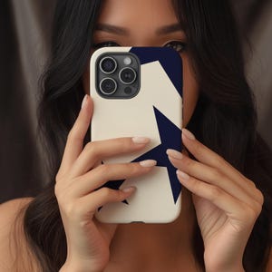 May include: A white phone case with a navy blue star design. The case has a smooth finish and features a camera cutout. The design is a bold, geometric pattern. The case is held in front of a person's face.