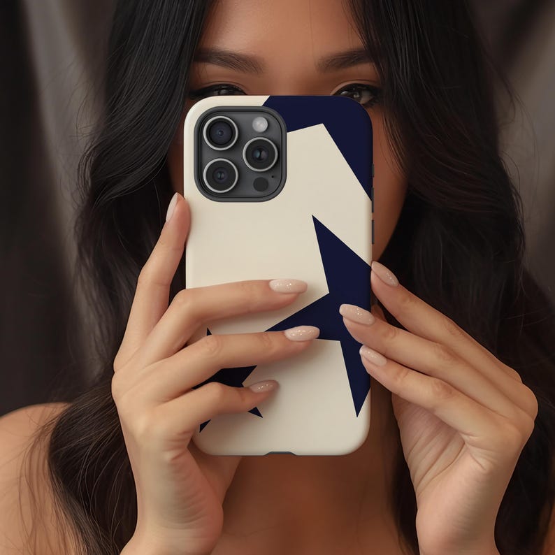 May include: A white phone case with a navy blue star design. The case has a smooth finish and features a camera cutout. The design is a bold, geometric pattern. The case is held in front of a person's face.