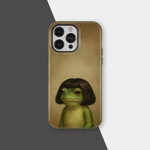 Puede incluir: Funda de teléfono con una ilustración caprichosa de una rana verde con una peluca marrón oscuro. La funda tiene un fondo beige y un acabado brillante, con la cámara y los botones visibles.