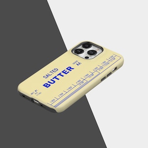 May include: A phone case with a butter-themed design. The case is light yellow with blue text that reads "SALTED BUTTER" and measurement markings. The case also has the words "GRADE AA" and "NET WT. 4 OZ. (113g)".