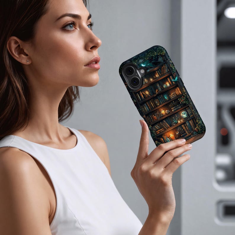 May include: A smartphone case featuring a detailed illustration of a bookshelf filled with books, candles, and other decorative items. The case has a dark background with green foliage and a moon. The case is held by a person.