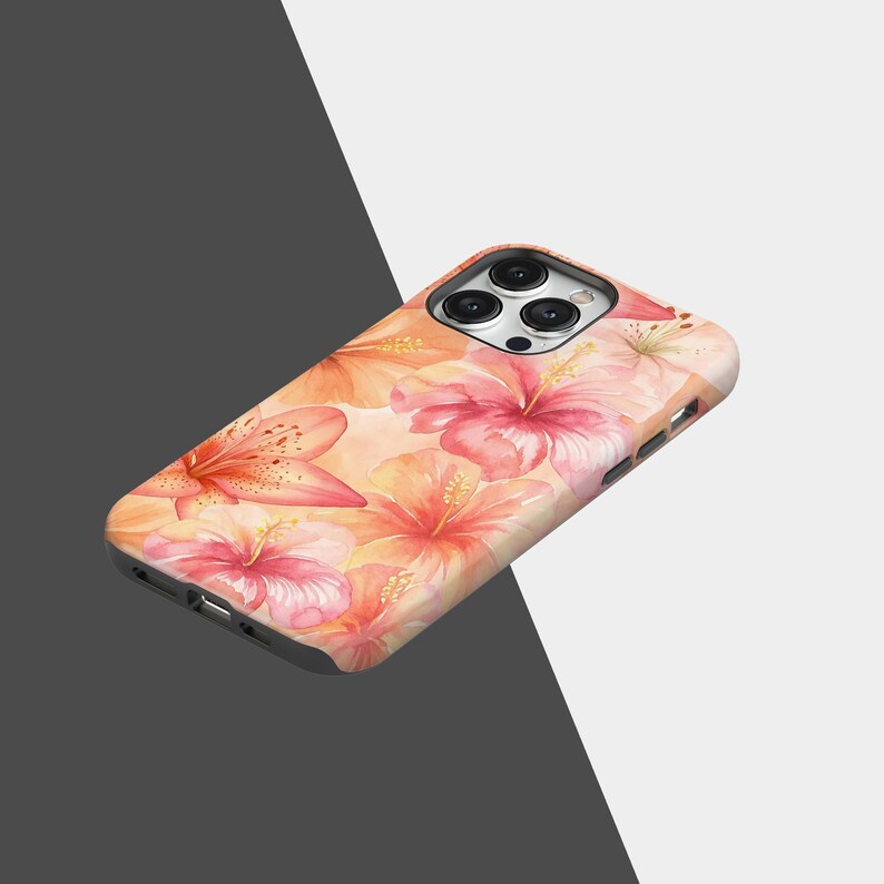 Puede incluir: Funda de tel&eacute;fono con un dise&ntilde;o floral en acuarela con flores de hibisco y lirios en tonos rosa, melocot&oacute;n y naranja. La funda tiene un acabado brillante y un recorte para la c&aacute;mara.