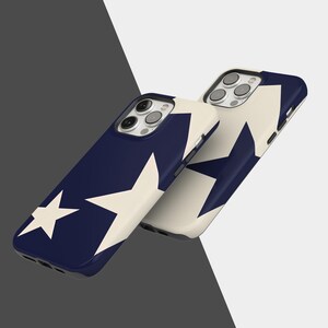 May include: Two navy blue phone cases with a cream-colored star design. The cases are shown at a slight angle, showcasing the camera cutouts and the star pattern. The background is a gradient of gray and white.