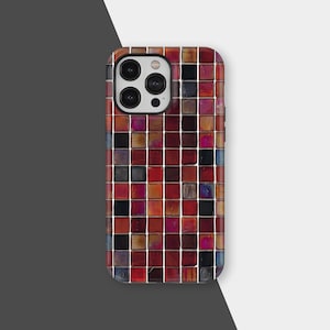 Puede incluir: Una funda de teléfono inteligente con un diseño de mosaico. La funda presenta un patrón de pequeñas baldosas cuadradas en tonos de rojo, naranja, marrón y negro, con líneas de lechada blancas. Las lentes de la cámara son visibles en la parte superior.