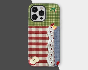 May include: A patchwork phone case featuring a green plaid top, red and white gingham middle, and denim side. Embellishments include a white lace trim, a red apple, a red cherry, and a green caterpillar.