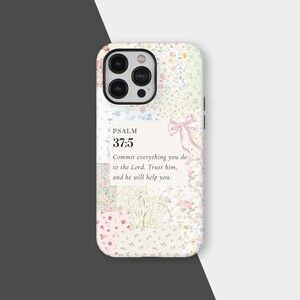 Puede incluir: Funda de teléfono con estampado floral con el texto "PSALM 37:5" y una cita: "Encomienda al Señor todo lo que haces. Confía en él, y él te ayudará." La funda tiene un lazo rosa claro.