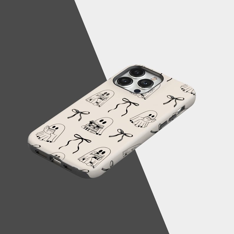 May include: A cream-colored phone case featuring a repeating pattern of black and white ghost illustrations and black bows. The case has a glossy finish and is designed to fit a smartphone, with cutouts for the camera and buttons.
