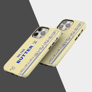May include: Two phone cases with a butter-themed design. The cases are light yellow with blue text that reads "SALTED BUTTER" and measurement markings. The cases have a net weight of 4 oz (113g).