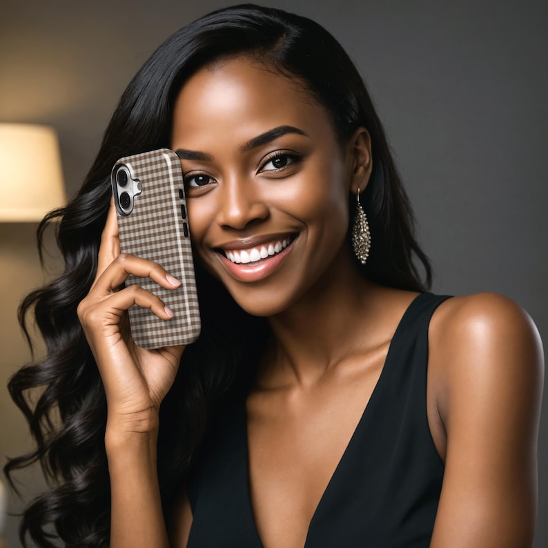 May include: A brown and white checkered phone case held by a person. The phone case is on a smartphone. The person is wearing a black dress and has long, dark hair. The background is a neutral gray.