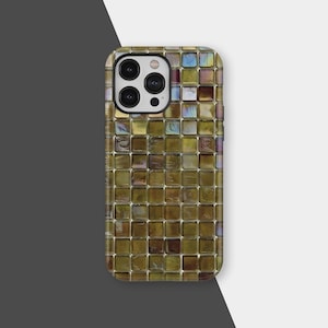 Puede incluir: Una funda de teléfono con un diseño de mosaico. La funda presenta un patrón de pequeñas baldosas cuadradas en tonos dorados, marrones e iridiscentes. Las lentes de la cámara son visibles en la parte superior.