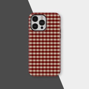 Könnte beinhalten: Eine Handyhülle mit einem rot-beigen Vichy-Muster. Die Hülle hat ein schwarzes Kameramodul und eine glatte, glänzende Oberfläche. Das Design ist ein klassischer, zeitloser Stil.