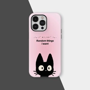 Puede incluir: Funda de teléfono rosa con una ilustración de gato negro con ojos y bigotes blancos. El texto "Random things I want" está impreso encima del gato. La funda tiene un módulo de cámara negro.