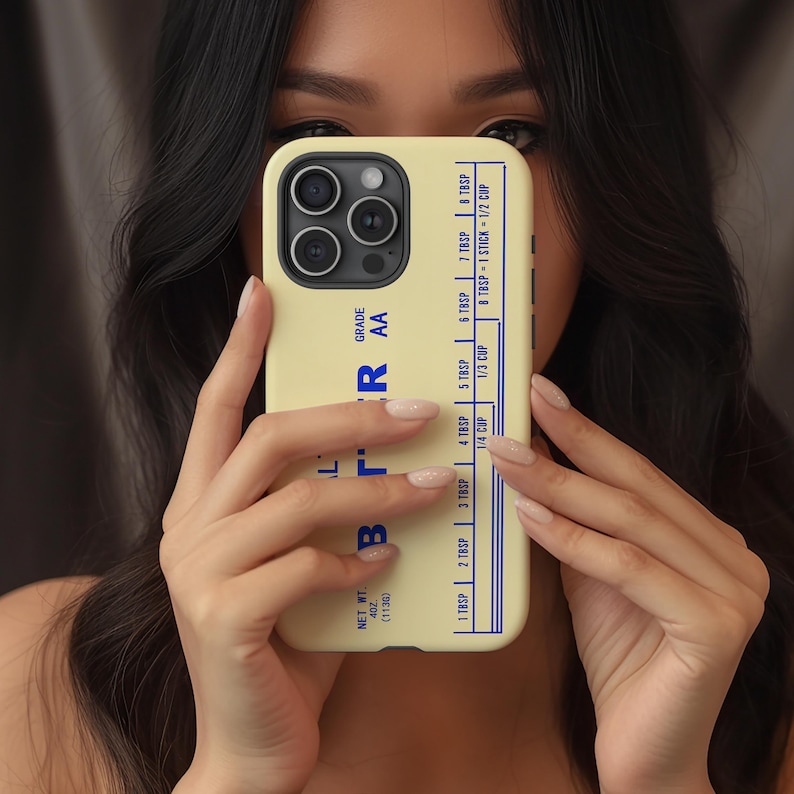 May include: A light yellow phone case with a blue butter measurement chart. The case features the word "BUTTER" in blue, along with measurements for tablespoons and cups. The phone case is held in front of a person.