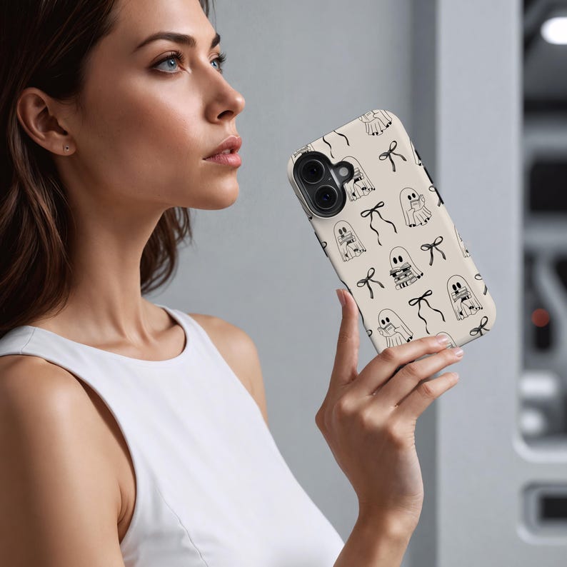 May include: A beige phone case with a repeating pattern of black line-drawn ghosts and bows. The case has a glossy finish and a camera cutout. The design is simple and whimsical, perfect for Halloween or everyday use.