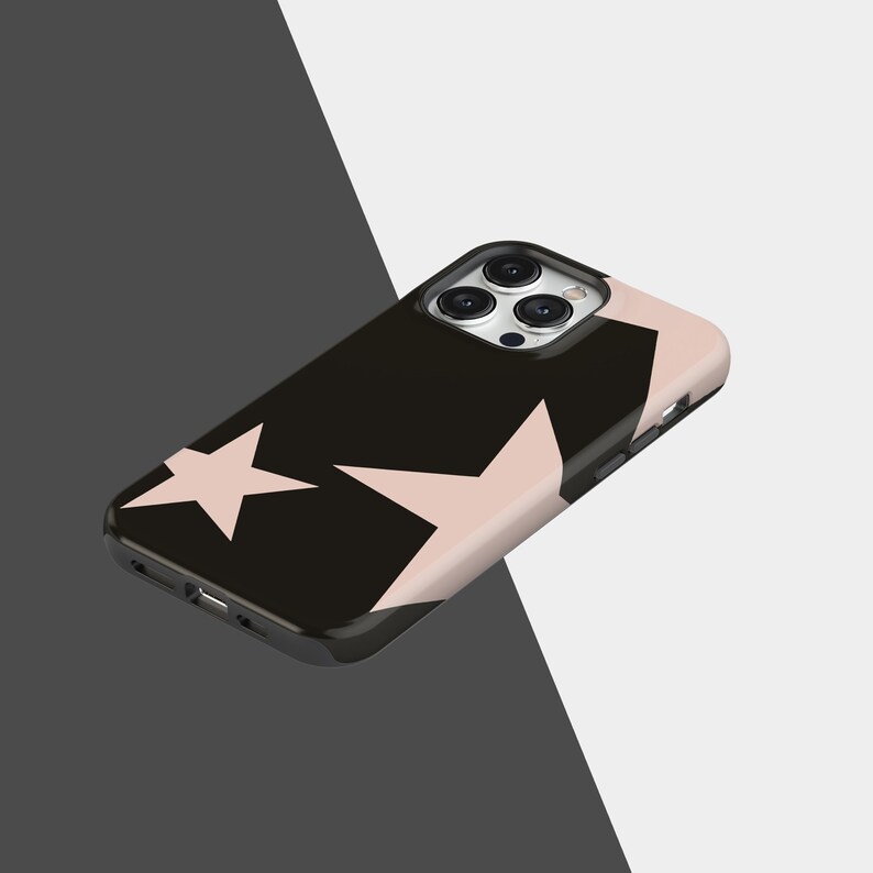May include: A black phone case with a pink star pattern. The case has a glossy finish and a raised edge around the camera. The design features two large, light pink stars against a black background. The case is designed for a smartphone.