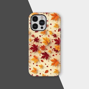 Puede incluir: Una funda de teléfono con un diseño otoñal. La funda presenta un patrón de hojas de arce rojas, naranjas y amarillas sobre un fondo crema. Pequeños corazones rojos también están dispersos por el diseño.