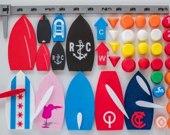 May include: A collection of flat, boat-shaped game pieces in various colors and designs, including anchors and symbols, alongside circular numbered tokens and directional arrows, arranged next to a 3-inch gray plastic caliper measuring tool.