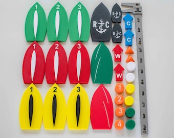 May include: A collection of colorful boating navigation aids, including green, red, and yellow buoys with numbers, arrows, and markers. Also includes gray markers with the letters "R C" and an anchor symbol, and a gray ruler.