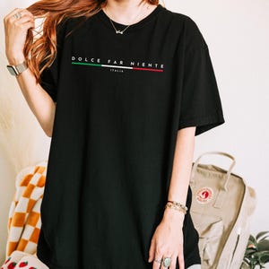 May include: Black t-shirt with the words "DOLCE FAR NIENTE" in white, with a green, white, and red stripe design. The word "ITALIA" is below the main text. The shirt is a casual, oversized style.