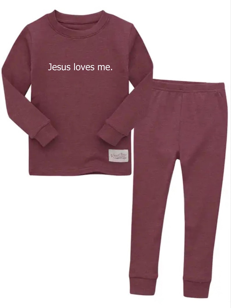 Puede incluir: Conjunto de pijama de dos piezas color granate. La parte superior de manga larga tiene el texto "Jesus loves me" en blanco. Los pantalones a juego tienen un dise&ntilde;o ajustado. Una peque&ntilde;a etiqueta est&aacute; cosida en la parte inferior de la parte superior.