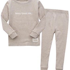 Puede incluir: Un conjunto de pijama de dos piezas en color beige claro. La parte superior de manga larga tiene el texto "Jesus loves me." Los pantalones a juego tienen un dise&ntilde;o ajustado. El conjunto est&aacute; hecho de un material suave y c&oacute;modo.