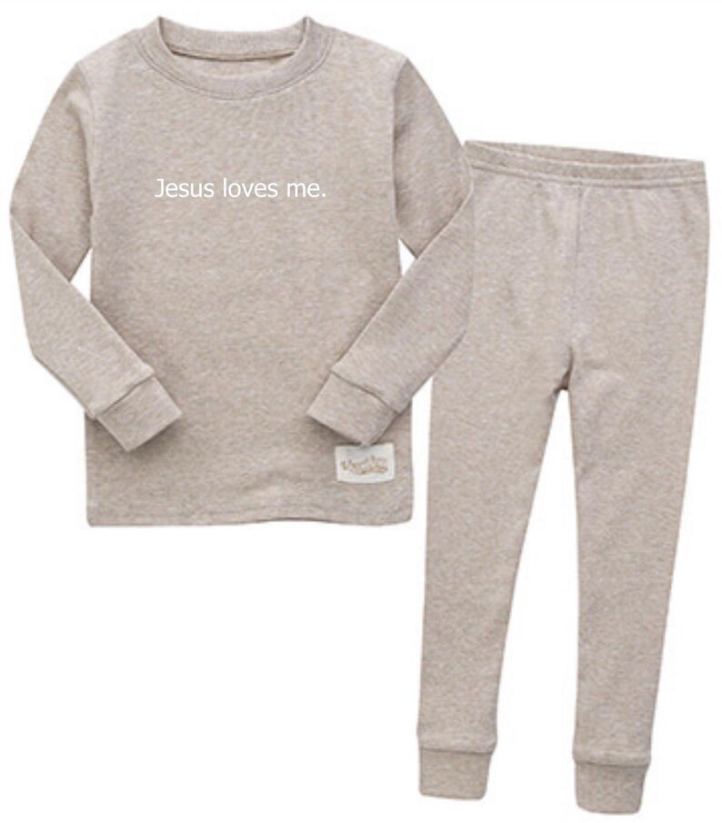 Puede incluir: Un conjunto de pijama de dos piezas en color beige claro. La parte superior de manga larga tiene el texto "Jesus loves me." Los pantalones a juego tienen un dise&ntilde;o ajustado. El conjunto est&aacute; hecho de un material suave y c&oacute;modo.