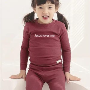 Puede incluir: Conjunto de camisa de manga larga y pantal&oacute;n burdeos. La camisa tiene el texto "Jesus loves me". El conjunto est&aacute; hecho de un material suave y es adecuado para ni&ntilde;os.