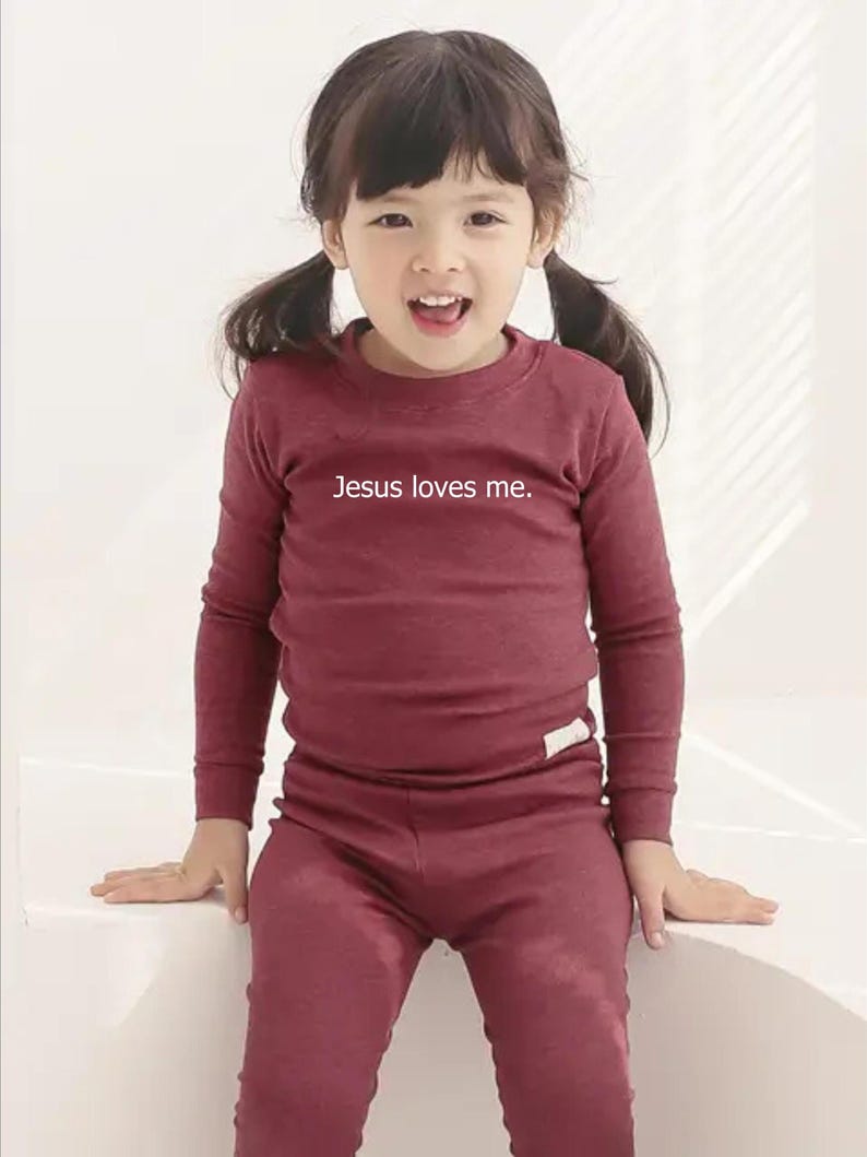 Puede incluir: Conjunto de camisa de manga larga y pantal&oacute;n burdeos. La camisa tiene el texto "Jesus loves me". El conjunto est&aacute; hecho de un material suave y es adecuado para ni&ntilde;os.