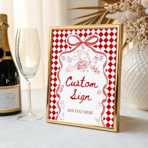 Könnte beinhalten: Ein goldgerahmtes Schild mit einem rot-weiß karierten Muster. Das Schild hat ein rotes Schleifendesign und die Worte "Custom Sign" in roter Schrift. Das Schild enthält Illustrationen von Pizza, Käse und anderen Lebensmitteln. Der Text "ADD TEXT HERE" ist ebenfalls enthalten.