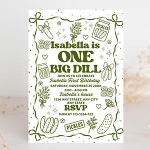 May include: A white invitation with a green border and text. The text reads "Isabella is ONE BIG DILL" and invites guests to Isabella's first birthday party. The design includes pickle illustrations.