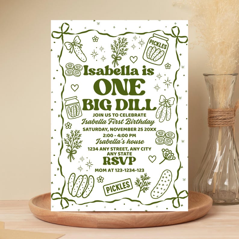 May include: A white invitation card with a green border and text. The text reads "Isabella is ONE BIG DILL" with details for a first birthday party, including the date, time, and location. Decorative pickle illustrations surround the text.