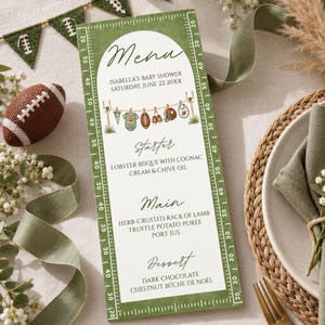 Könnte beinhalten: Eine rechteckige Menükarte mit einem grünen Footballfeld-Rand und Yard-Markierungen. Die weiße Mitte zeigt den Text Menu, Isabella's Baby Shower, Saturday, June 22 20XX, Starter, Main und Dessert mit den jeweiligen Speisen.