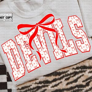 Puede incluir: Una sudadera gris claro con la palabra "DEVILS" en letras rojas grandes. Las letras están rellenas con un patrón de lazos y corazones rojos. Un lazo rojo grande está centrado sobre la palabra. También se ven las palabras "descarga digital" y "diseñado por designwinco".