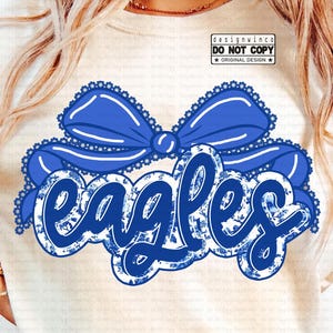 May include: A cream-colored t-shirt featuring a large blue bow and the word "EAGLES" in a blue floral design. The shirt also includes the text "digital download" and "DESIGNED BY DESIGNWINCO".