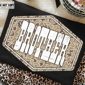 May include: Black t-shirt with a distressed, geometric design that reads "BROTHER" in white block letters. The design has a camouflage pattern in shades of brown and tan. The words "DO NOT COPY" and "ORIGINAL DESIGN" are also visible.