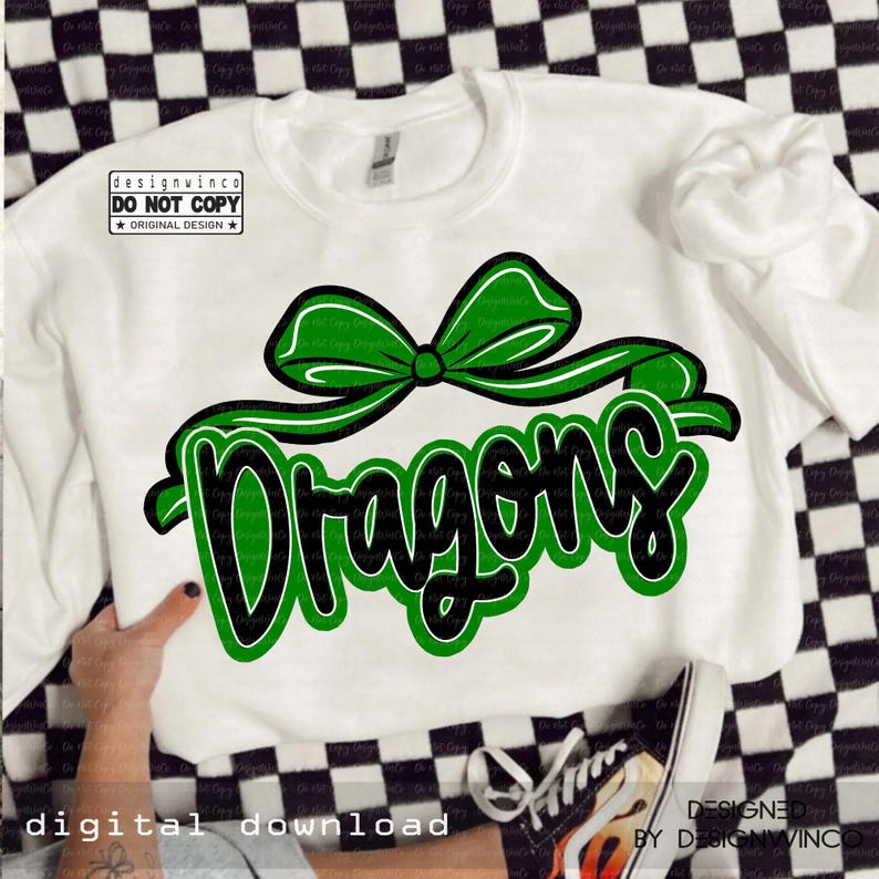 Op de afbeelding: Witte sweatshirt met een groene strik en het woord "Dragons" in een zwart-groen ontwerp. De sweatshirt heeft de tekst "designwinco DO NOT COPY ORIGINAL DESIGN" in de linkerbovenhoek. De woorden "DIGITALE DOWNLOAD" staan onderaan.