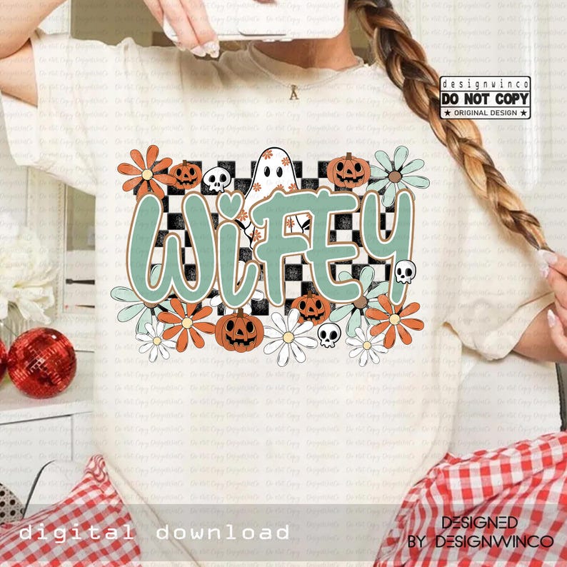 May include: Cream-colored t-shirt with a graphic design featuring the word "Wifey" in teal, surrounded by pumpkins, flowers, a ghost, and skulls. The design is set against a black and white checkered background.