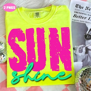 Puede incluir: Una camiseta amarilla neón con las palabras "SUN" en letras grandes de color rosa brillante y "shine" en una fuente cursiva de color turquesa. La camiseta, con una etiqueta Comfort Colors, se muestra sobre una superficie a cuadros rosa y blanca.