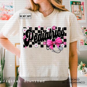 May include: Cream-colored t-shirt featuring the word "Pediatrics" in a black, cursive font over a black and white checkered background. Pink bow and stethoscope graphic. White daisy and pink star accents. Text: "designwinco DO NOT COPY ORIGINAL DESIGN".