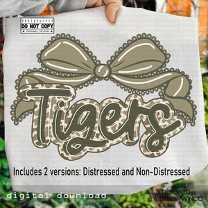 May include: A digital download design featuring the word "Tigers" in a camouflage pattern, framed by a decorative bow. The design includes two versions: distressed and non-distressed. The text "designwinco DO NOT COPY ORIGINAL DESIGN" is also present.