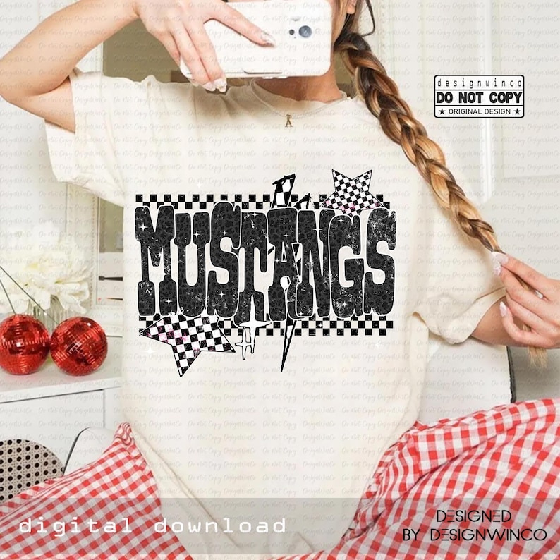 May include: Cream-colored t-shirt featuring the word "MUSTANGS" in a bold, black, bubble-style font with a checkered pattern. The design includes star and lightning bolt graphics. The text "DESIGNED BY DESIGNWINCO" is also visible.