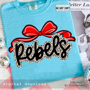 May include: A light blue t-shirt featuring a large red bow and the word "Rebels" in a black, leopard print font. The shirt also has the text "digital download" and "DESIGNED BY DESIGNWINCO".