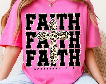 May include: A bright pink t-shirt with the word "FAITH" in a bold, black font. A cross with a leopard print design is centered on the shirt. The text "EPHESIANS 2:8" is printed below the word "FAITH".
