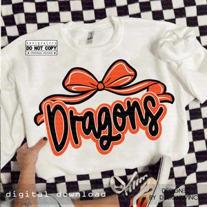 Op de afbeelding: Witte sweatshirt met het woord "Dragons" in oranje en zwarte letters, bekroond met een oranje strik. De tekst "designwinco DO NOT COPY ORIGINAL DESIGN" staat linksboven. De woorden "DIGITAL DOWNLOAD" staan linksonder.