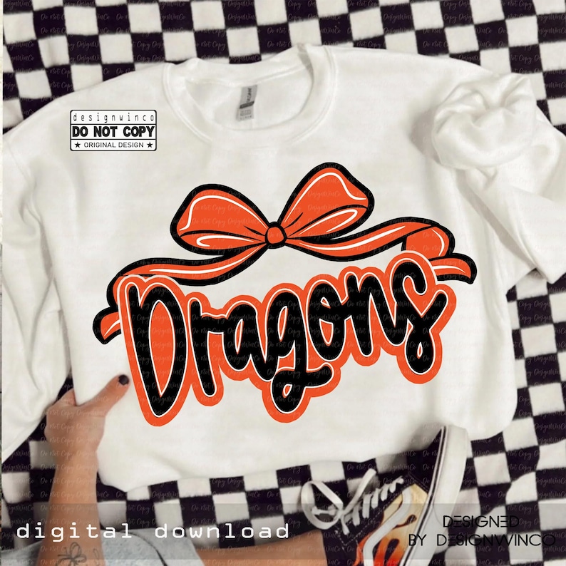 Op de afbeelding: Witte sweatshirt met het woord "Dragons" in oranje en zwarte letters, bekroond met een oranje strik. De tekst "designwinco DO NOT COPY ORIGINAL DESIGN" staat linksboven. De woorden "DIGITAL DOWNLOAD" staan linksonder.