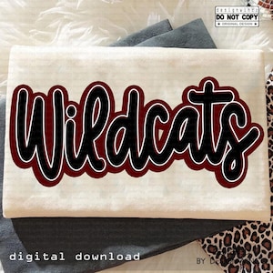 Peut inclure: Un t-shirt crème plié avec le mot "Wildcats" en noir gras, souligné de blanc et rempli de bordeaux. Les mots "digital download" sont en bas. Le design est sur un t-shirt plié.