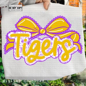 May include: White fabric with a yellow and purple design. The word "Tigers" is in yellow script with a floral pattern, outlined in purple. A yellow bow with purple trim sits above the word. The text "designwinco" and "digital download" are also visible.
