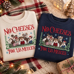 Könnte beinhalten: Zwei Rundhals-Sweatshirts, eines in Creme und eines in Marineblau, mit einer Stickerei von fünf Mäusen in Winterkleidung. Der Text NO CHEESES FOR US MEECES ist in Rot gehalten, umrahmt von grünen Zierlinien und kleinen blauen Schneeflocken.